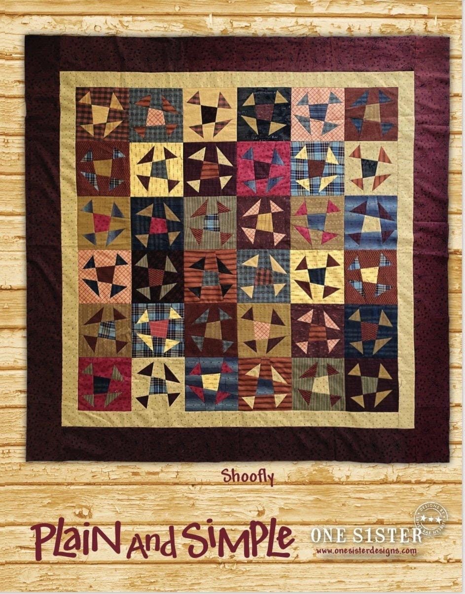 May include: Shoofly quilt pattern from One Sister Designs. This quilt features a patchwork design with various shades of brown, beige, and blue fabrics. The blocks are arranged in a grid pattern, creating a visually appealing design. The quilt is bordered with a darker brown fabric. The text &#39;Plain and Simple&#39; is displayed below the quilt image, along with the company logo and website address.